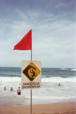 Waimea Bay sign: Dangerous shorebreak.  Swimmers in the distance.