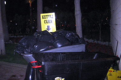 Sign saying "Kettle Corn" with an arrow pointing downward... placed on top of a pile of trash bags.