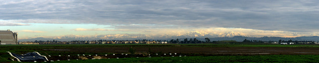 Wider view of the same snow covered mountains lit up by the sun, with clouds above them. 