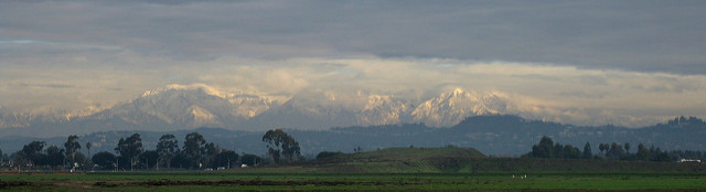 Snow covered mountains lit up by the sun, with clouds above them.