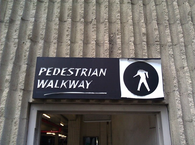Pedestrian Walkway sign with the paint peeling so that the head is missing from the stick figure.