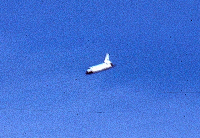 Small view of the space shuttle against a blue sky.