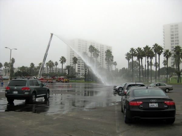 A hazmat team power-washes the parking lot from a fully-extended fire engine ladder.