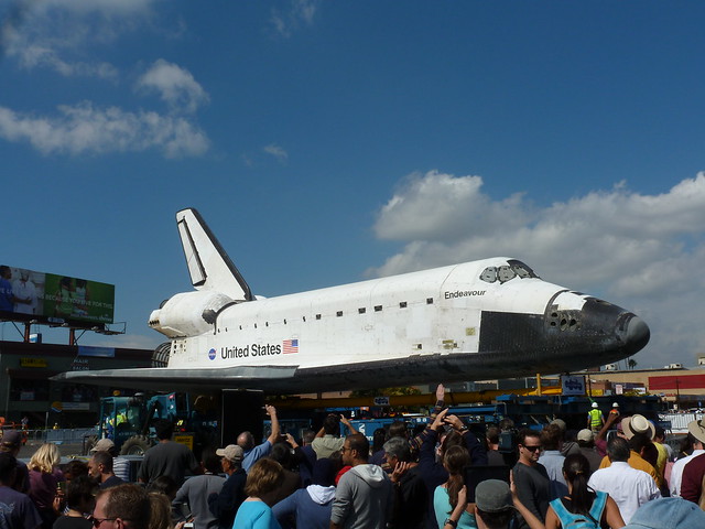 A crowd of people looking at the space shuttle on a sunny day.