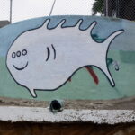 A cartoon-looking fish on the side of a round concrete structure. The fish has a smiling mouth and three eyes.