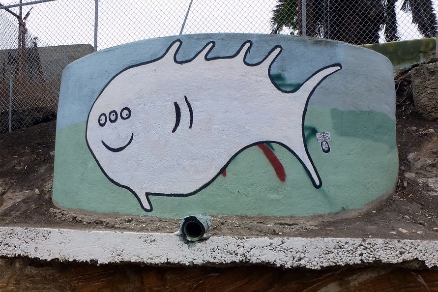 A cartoon-looking fish on the side of a round concrete structure. The fish has a smiling mouth and three eyes.