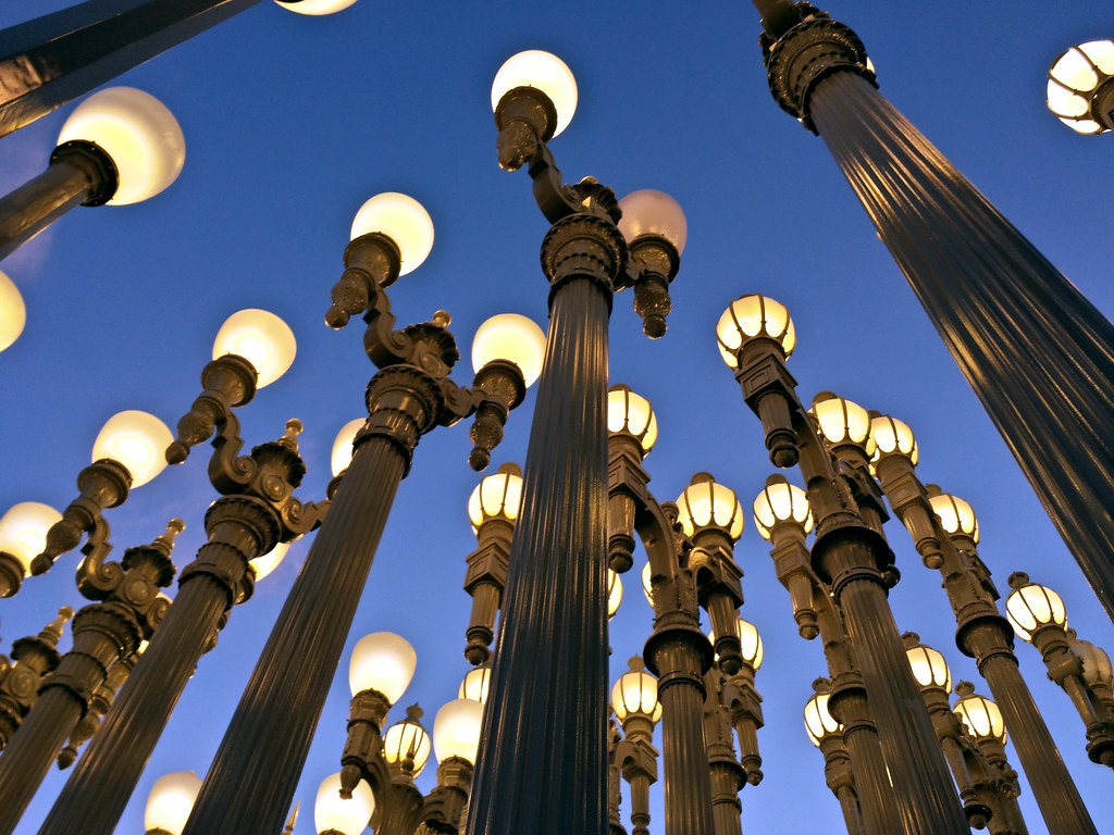 Looking up at a whole bunch of old-fashioned lampposts clustered together, ridged columns and lit globes seen against a dark blue sky.