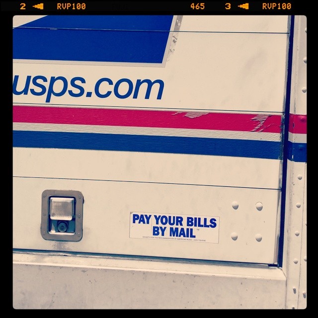 Postal truck with bumper sticker: Pay Your Bills By Mail!