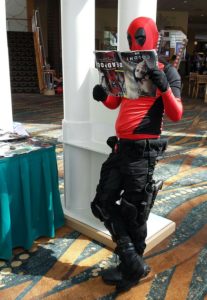 Deadpool leans against a column, reading a magazine about himself. Upside-down.