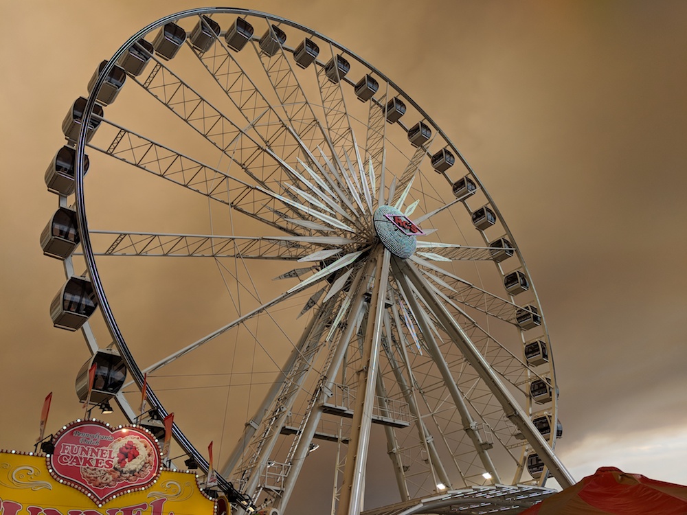 [Looking up at a Ferris Wheel against clouds of yellowish-brown smoke.]