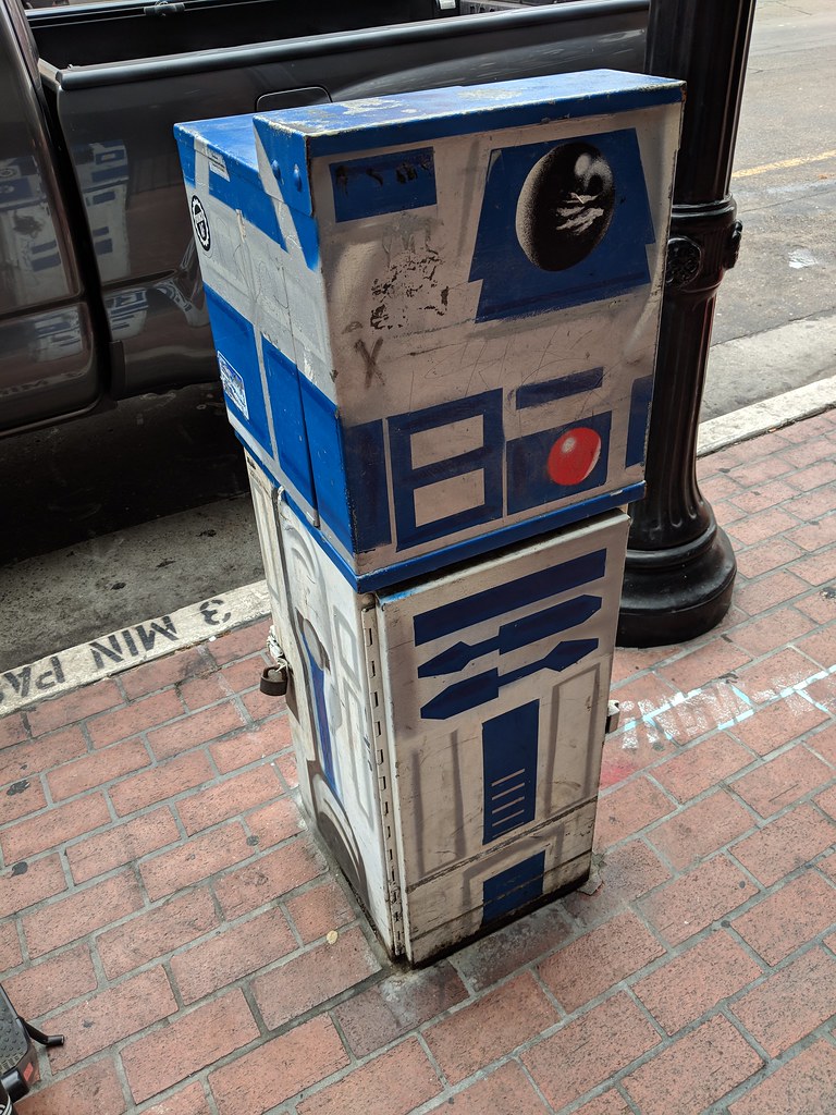 Rectangular utility box on a city street, about a meter high, painted to look like R2-D2 from Star Wars.