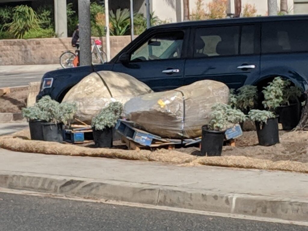 Two boulders strapped onto wooden pallets by the side of the street. The pallets have been crushed by the weight.