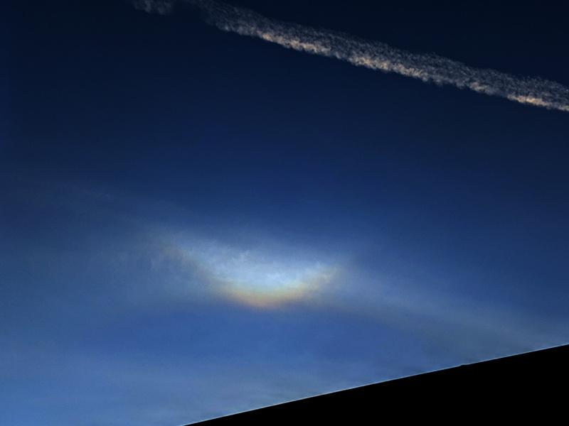 A diffuse bright V-shaped light in the sky, slightly redder on the lower edge, with a faint arc of light extending downward from the center.