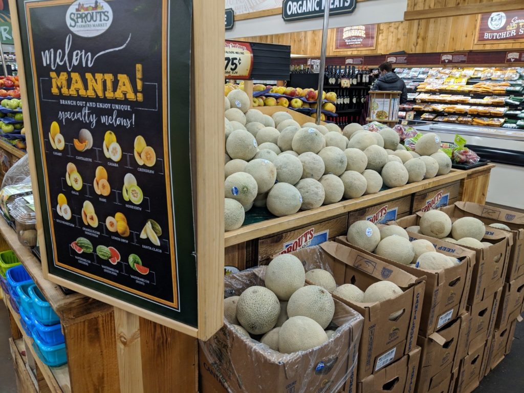 Grocery store display with a sign showing how to identify a dozen types of melons.and a shelf covered with nothing but cantaloupe.