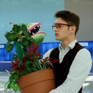 Man dressed as Seymour with a prop Audrey II from Little Shop of Horrors