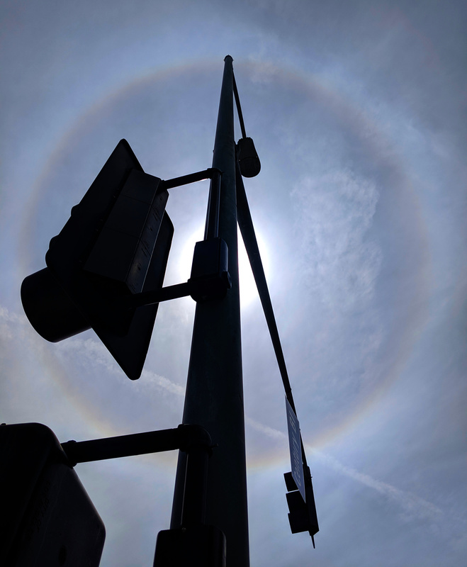 A circular halo of light around the sun, with a silhouetted traffic signal.