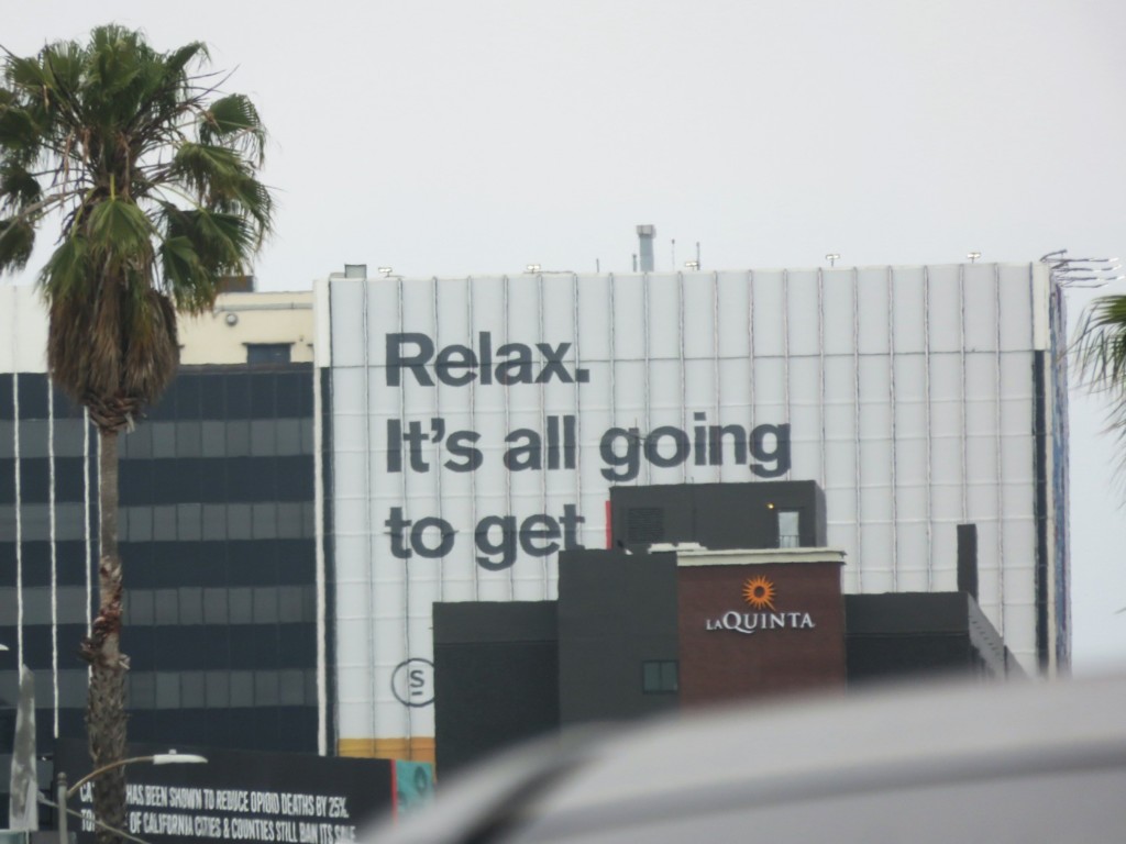 Giant sign saying Relax. It's all going to get - and then the last word is blocked by a black rectangle on top of another building.