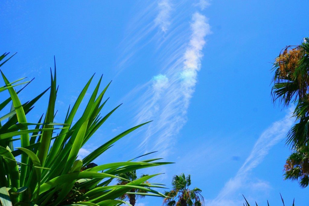 Wispy cirrus clouds/contrails against a blue sky, with a rainbow-colored section.