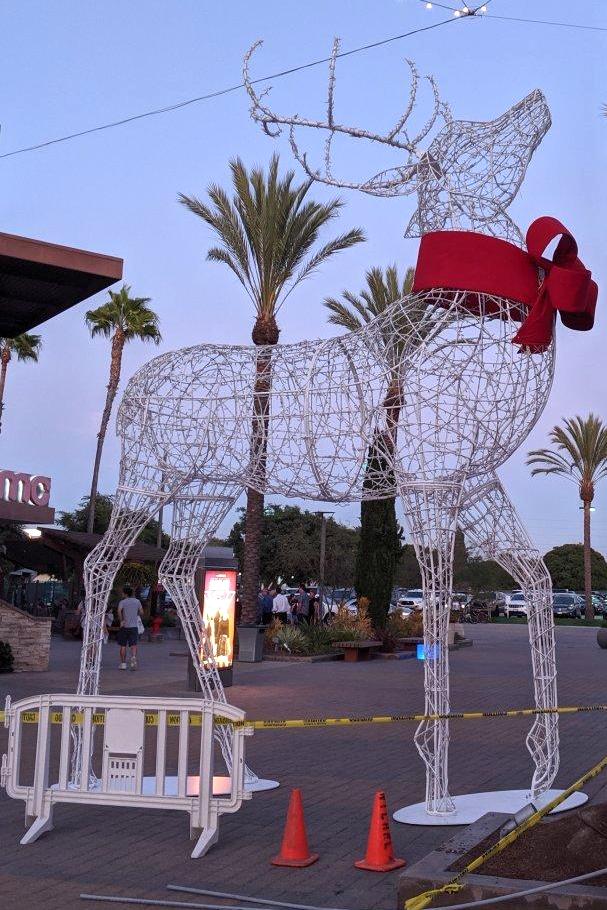 A wireframe reindeer sculpture outdoors on a brick floor, surrounded by palm trees.