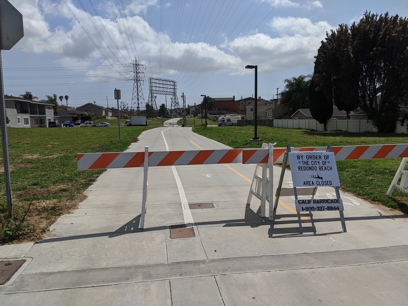 Barrier in front of a bike path with wide swaths of grass to either side.