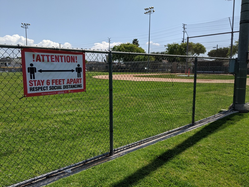 Baseball field with a sign on the fence saying ATTENTION: STAY 6 FEET APART