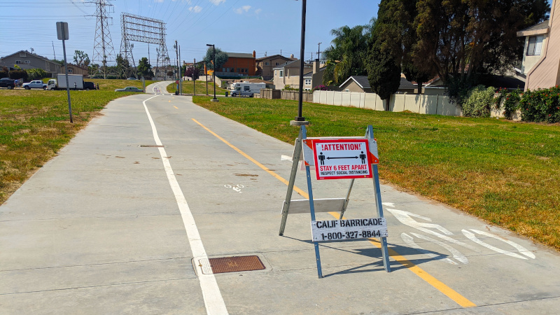 Bike path on a sunny day with a sign saying to maintain 6 feet of distance between people.