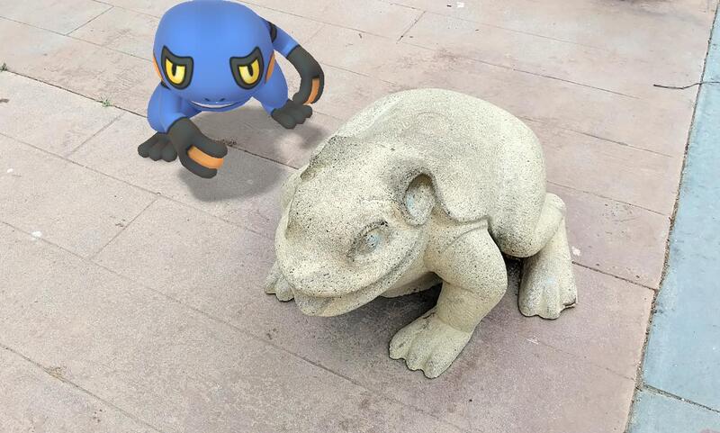 A frog-like Pokemon next to a real statue of a frog.
