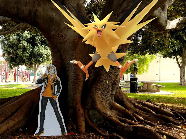 Cardboard stand-up of Spark, a human character from Pokemon, in front of a tree, with a lightning/bird-like Pokemon superimposed over the image.