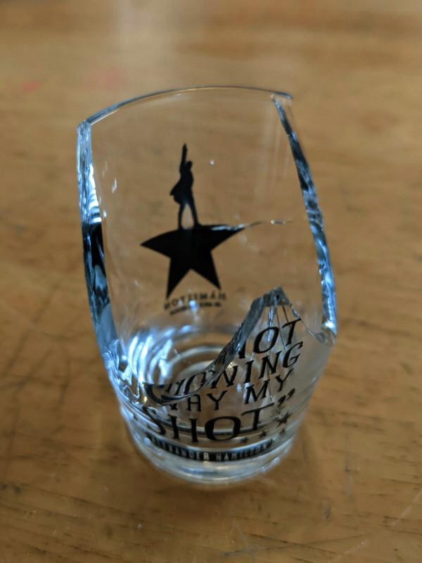Broken shot glass with Hamilton logo and what's left of the quote, "I am not throwing away my shot!"