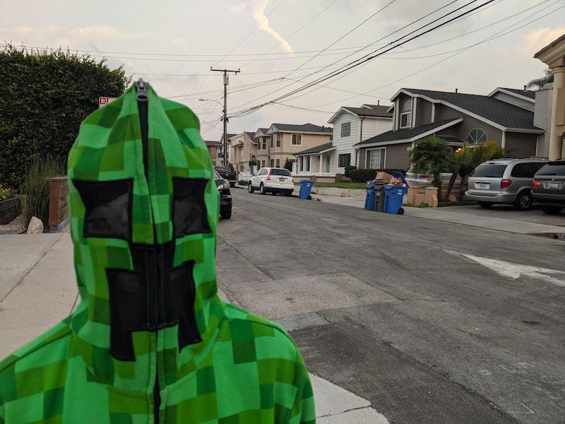 Someone in a green hoodie sweatshirt that zips all the way up turning the mask into a Minecraft Creeper face.