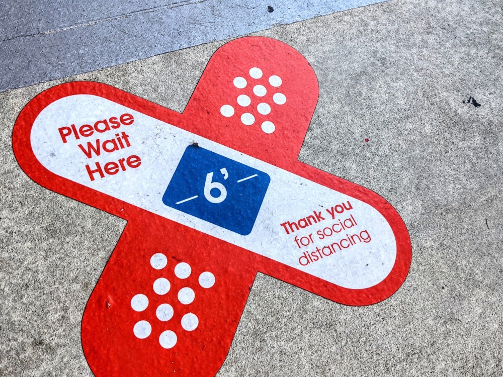A sticker on the sidewalk in the form of crossed bandages to help people maintain distance while waiting in line.