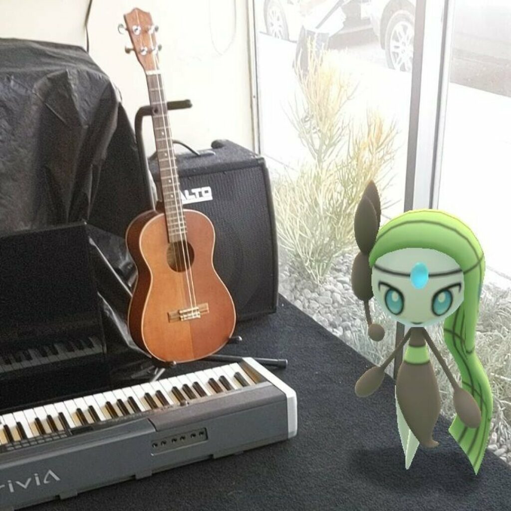 Photo of a guitar leaning against a speaker, next to a piano-style keyboard, with a computer image of a green humanoid with a microphone headset styled like a treble cleff standing next to the instruments.