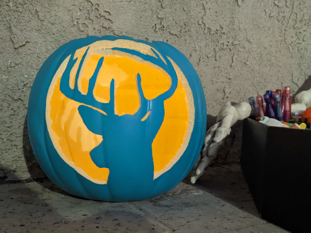 A teal pumpkin carved with the silhouette of a deer's head and antlers.