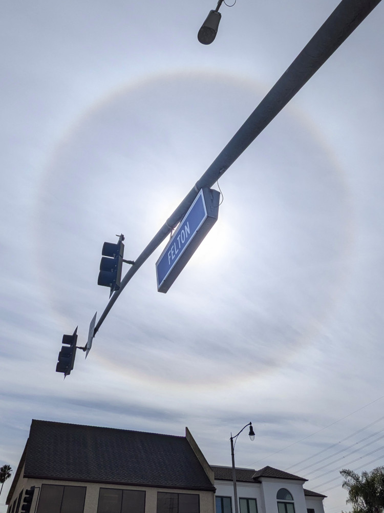 A bright ring surrounds the sun, which is blocked by an overhanging street sign.