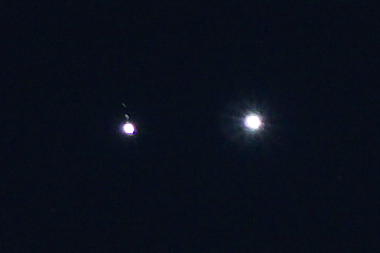 Closeup: two white circles against a dark blue background. The one on the right is bigger and has diffraction rays radiating from it. The one on the left doesn't, but there are two faint, blurry dots above it aligned with the disc.