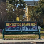 A bus stop bench with the slogan RENT IS TOO DAMN HIGH.