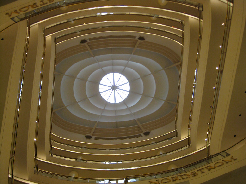 Looking straight up a central gallery with alternating straight and curved railings. The top is a circle surrounded by concentric ovals, resembling a giant eye looking down at the camera. Nordstrom can be read on the lowest visible railing.