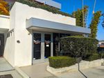 Storefront in a boxy-looking building with a low hedge and glass doors.