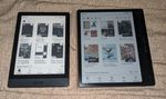 Two tablet devices, both with paper-like displays, both displaying a double-row of book covers. The first is a little shorter and wider than a mass-market paperback, and shows the book covers in black and grayscale. The second is a bit larger all around, plus it has a wider border on the right edge with a pair of buttons arranged vertically. It's also displaying its collection in color, if not very bright color.