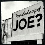 Stark black and white image of a sign painted directly on an outer wall. Wooden boards are visible next to it, and the top of a window frame below it. The sign reads 'How about a cup of' in cursive, and then in MUCH LARGER SANS-SERIF BLOCK LETTERS, 'JOE'.