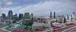 Panoramic view of a cityscape from a rooftop. Lower buildings with flat roofs, and in the distance taller buildings of all sorts of shapes. A few of the shorter ones clearly have old-fashioned facades, and you can juts make out the sail-like covering of the San Diego Convention Center.