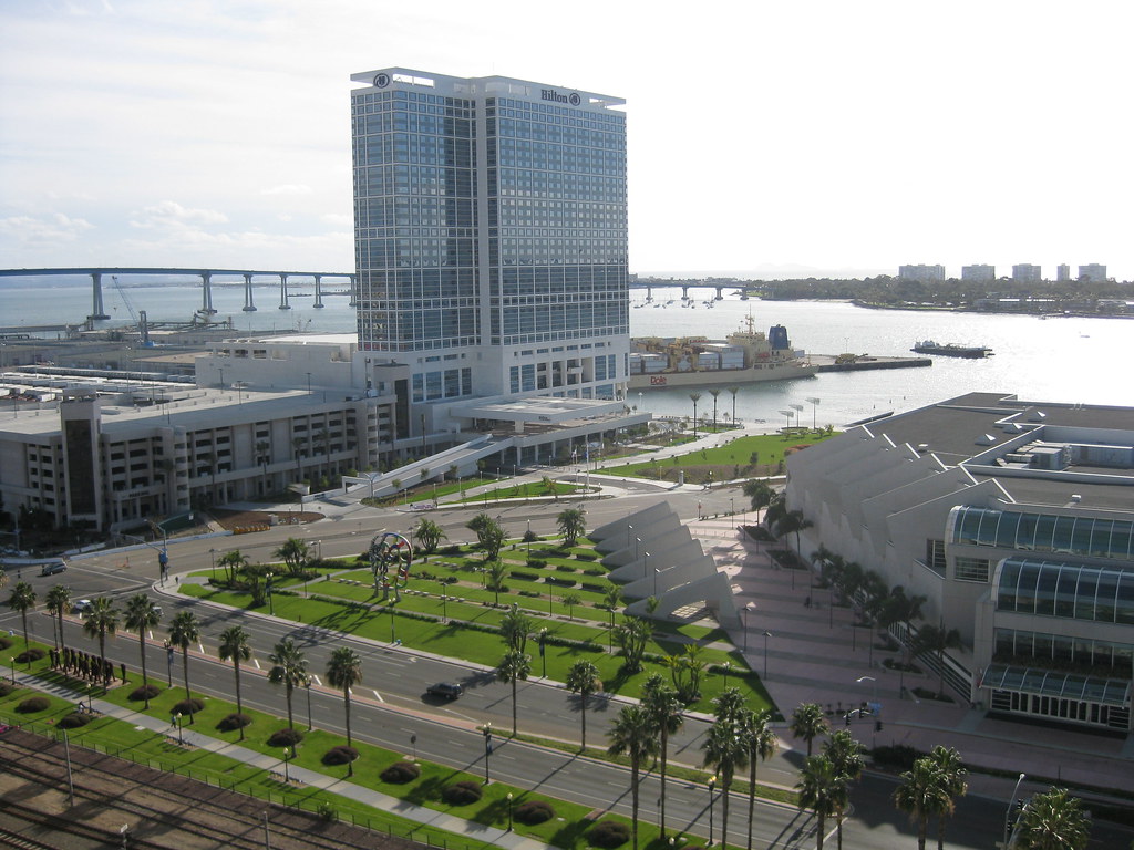 A tall building and a shorter one along a shoreline, seen from above, with grass between them.
