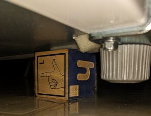 Underneath the refrigerator. a metal assembly wraps around the corner. A metal screw and a wide plastic cylinder with grip ridges are holding it to the unit.